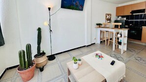 A modern living room with a flat-screen TV, a coffee table with plants, and a kitchen area with wooden cabinets and a black stove. - Cozy MEX-style apartment just steps from Reforma. (Ciudad de México)