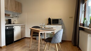 Een compacte keuken met houten kastjes, een magnetron en een kleine eettafel met twee stoelen.
