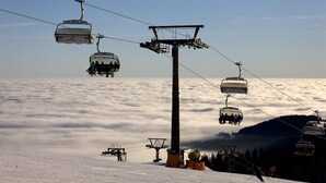 Een stoeltjeslift met gondels boven een besneeuwd landschap, daaronder een zee van wolken.