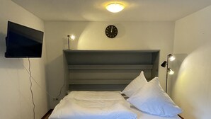 Een moderne slaapkamer met een bed, een flatscreen televisie aan de muur, een klok en een bedlampje.