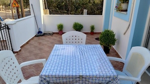 Eine Terrasse mit Tisch und Stühlen, Blumentöpfen und Blick auf die Straße.
