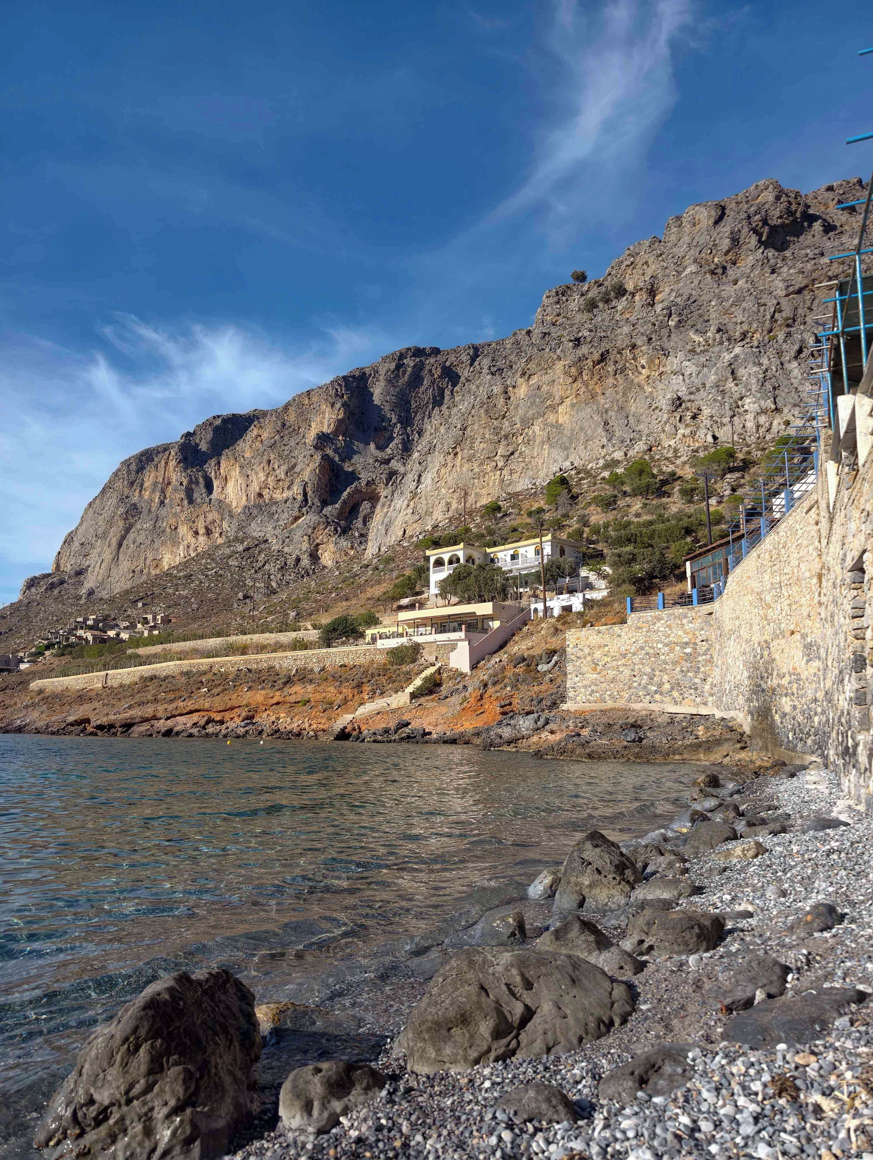 A coastal building with a stone facade, situated on a rocky shoreline with clear blue water.
