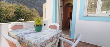 A terrace with a table and chairs, a potted plant, and a view of a mountain.