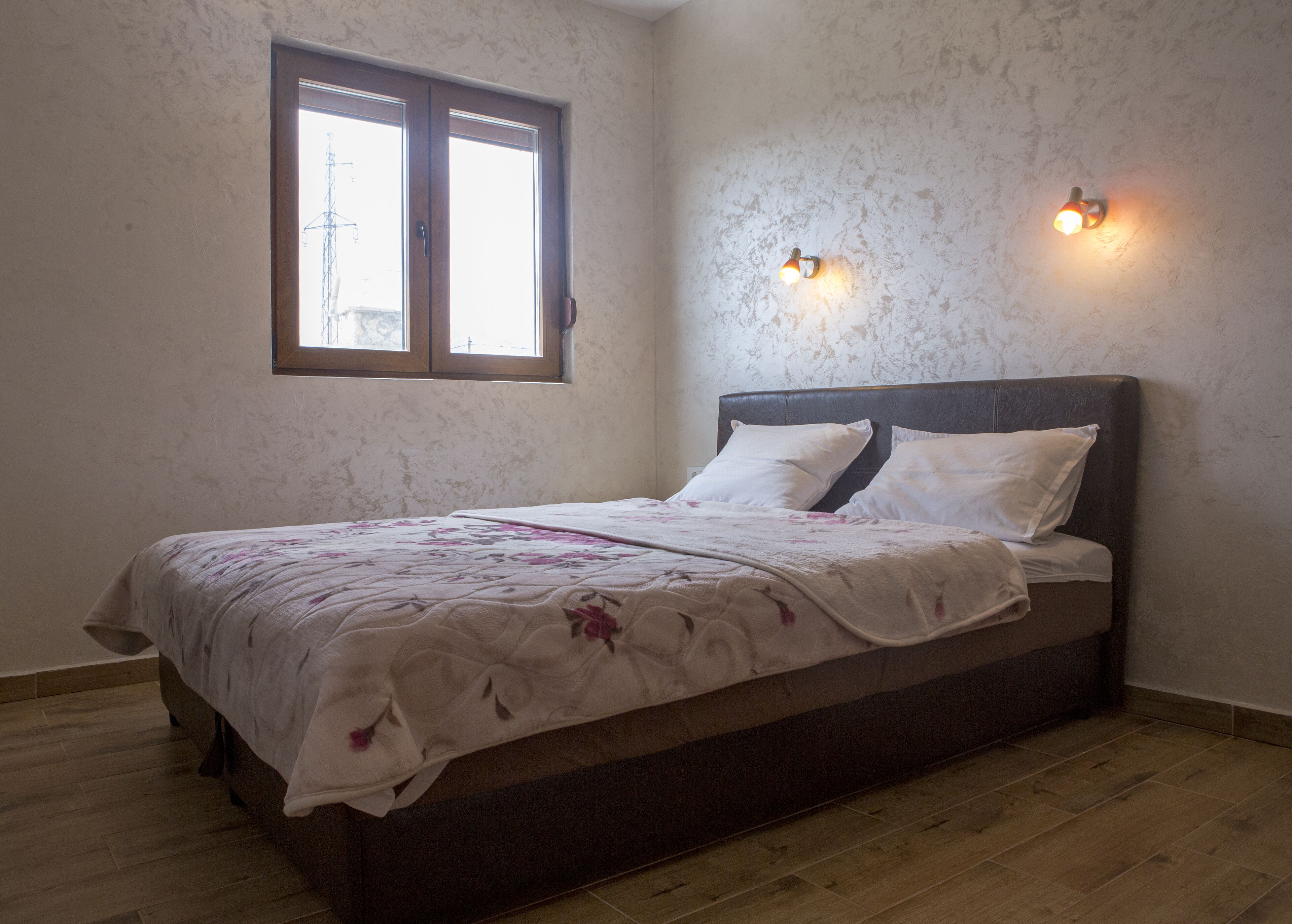 Una camera da letto con un letto, una finestra e due lampade fissate alla parete.