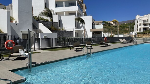 Une piscine avec des chaises longues, une bouée de sauvetage et un bâtiment moderne doté de balcons.