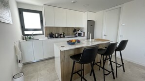 Une cuisine moderne avec des meubles blancs, un îlot central doté de tabourets, une fenêtre et un four à micro-ondes.