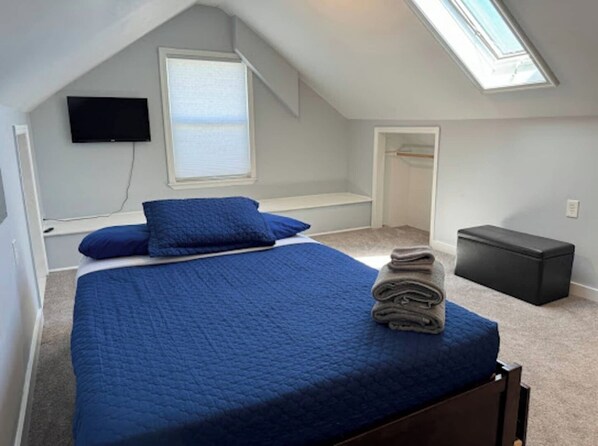 Un dormitorio con cama, televisión, tragaluz y vestidor.