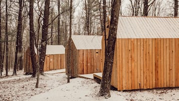 A wooden cabin with a metal roof, surrounded by trees and covered in snow.