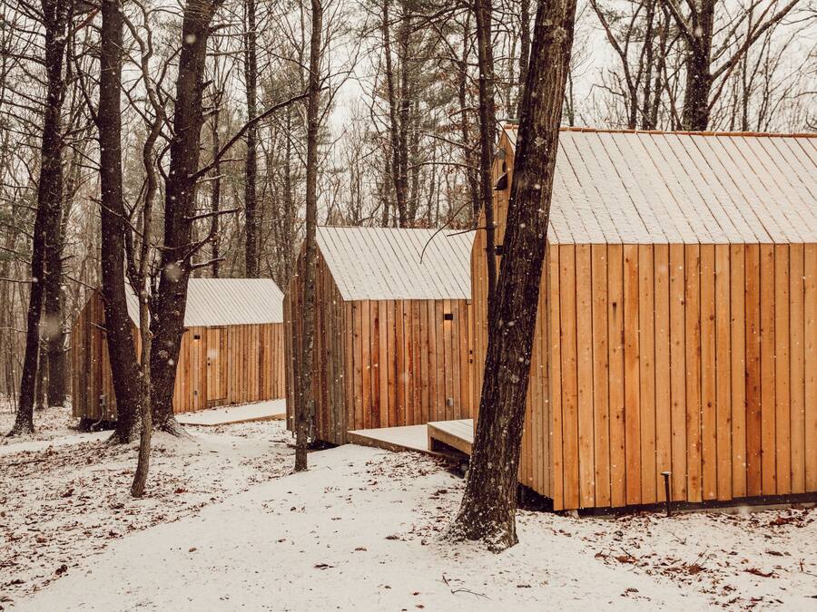 A wooden cabin with a metal roof, surrounded by trees and covered in snow.