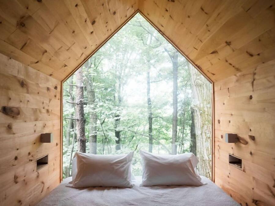 Una cabaña con ventana triangular, paredes de madera y una cama con almohadas.