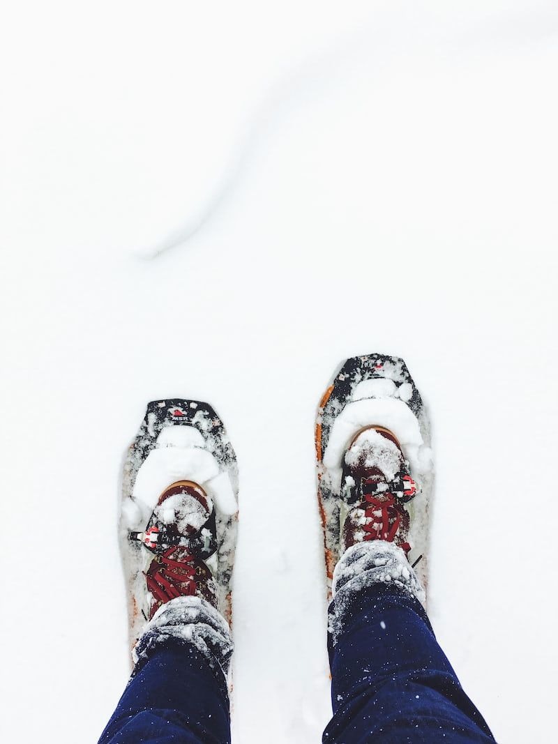 A pair of snow-covered shoes with red laces and a snowboard.