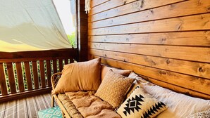 A wooden deck with a woven sofa, patterned cushions, and a hanging light fixture.