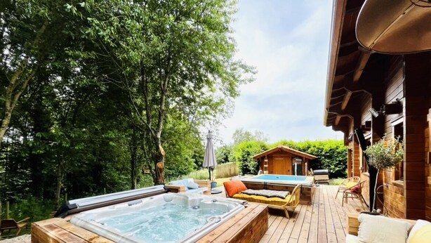 A wooden deck with a hot tub, outdoor seating, and a wooden cabin in the background.