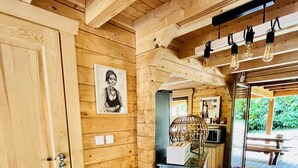 A wooden interior with a wooden chair, a door, a framed picture, a small table, and a bench outside.