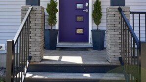 Een voorzichtszicht van een huis met een paarse deur, twee potplanten en een trap met zwarte leuningen.