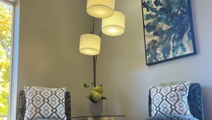 Een kamer met twee fauteuils, een glazen salontafel, een vloerlamp, een schilderij en een raam met uitzicht op bomen.