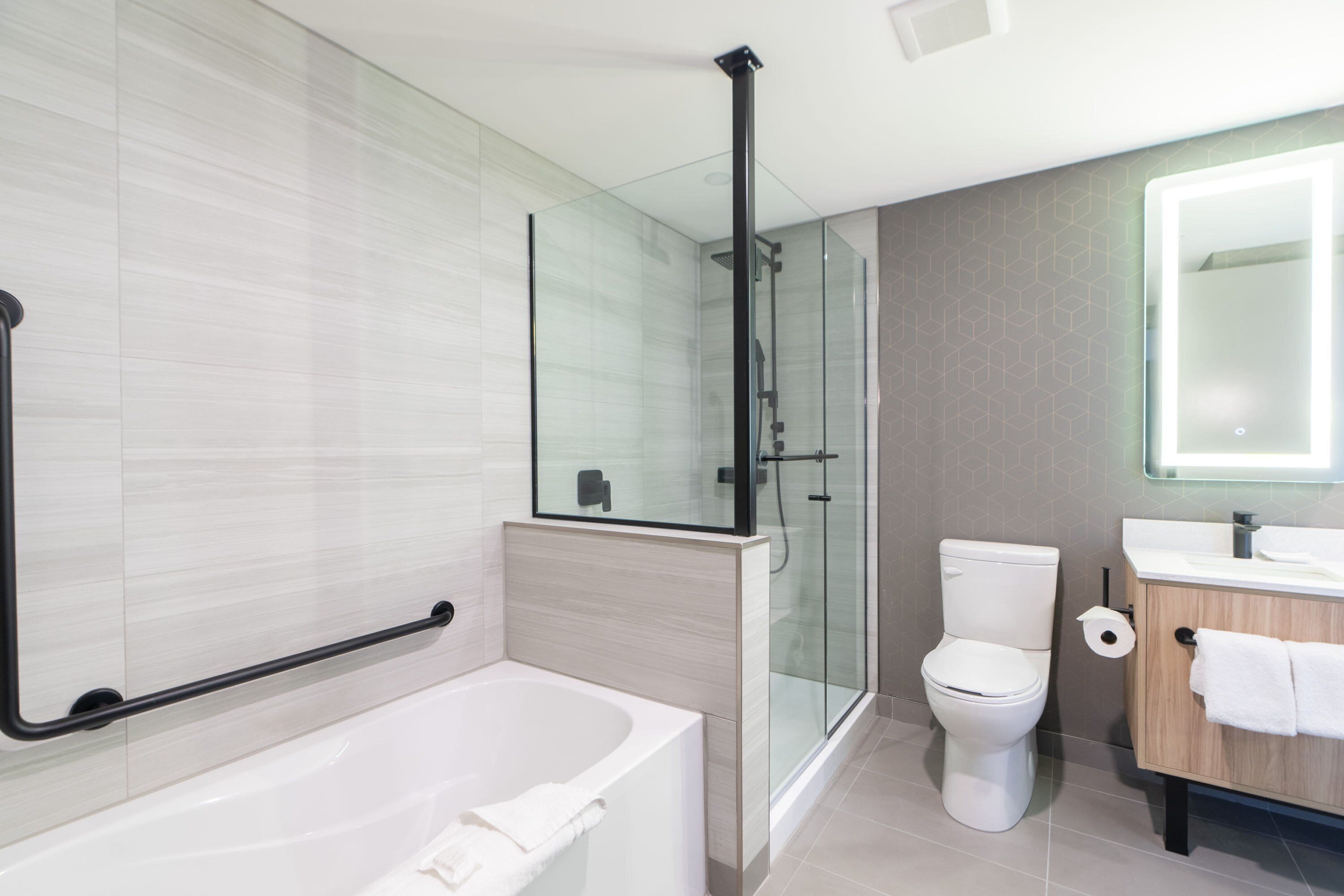 A modern bathroom with a glass shower enclosure, a white bathtub, a toilet, and a wooden vanity with a mirror.