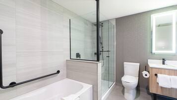 A modern bathroom with a glass shower enclosure, a white bathtub, a toilet, and a wooden vanity with a mirror.