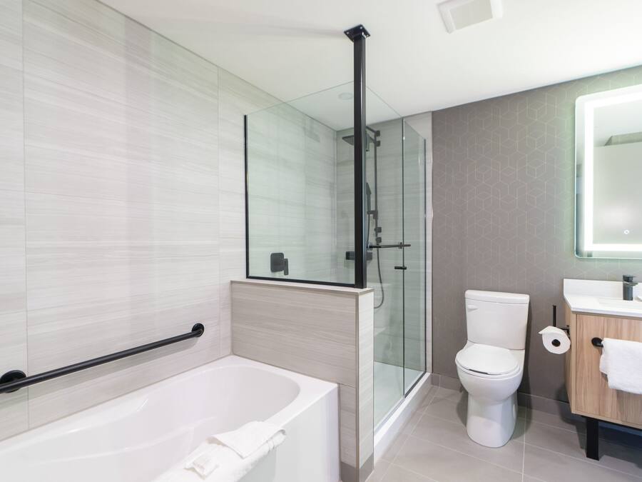 Un baño moderno con cabina de ducha de vidrio, bañera blanca, inodoro y tocador de madera con espejo.