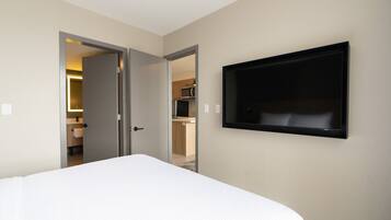 A hotel room with a bed, a television mounted on the wall, and an open door leading to a bathroom and kitchen area.