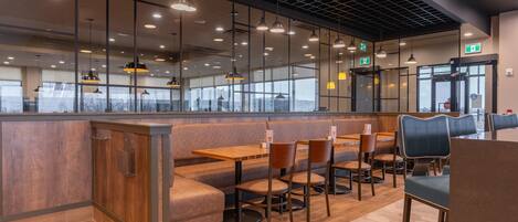Een modern restaurantinterieur met houten tafels, comfortabele zithoeken en hanglampen.