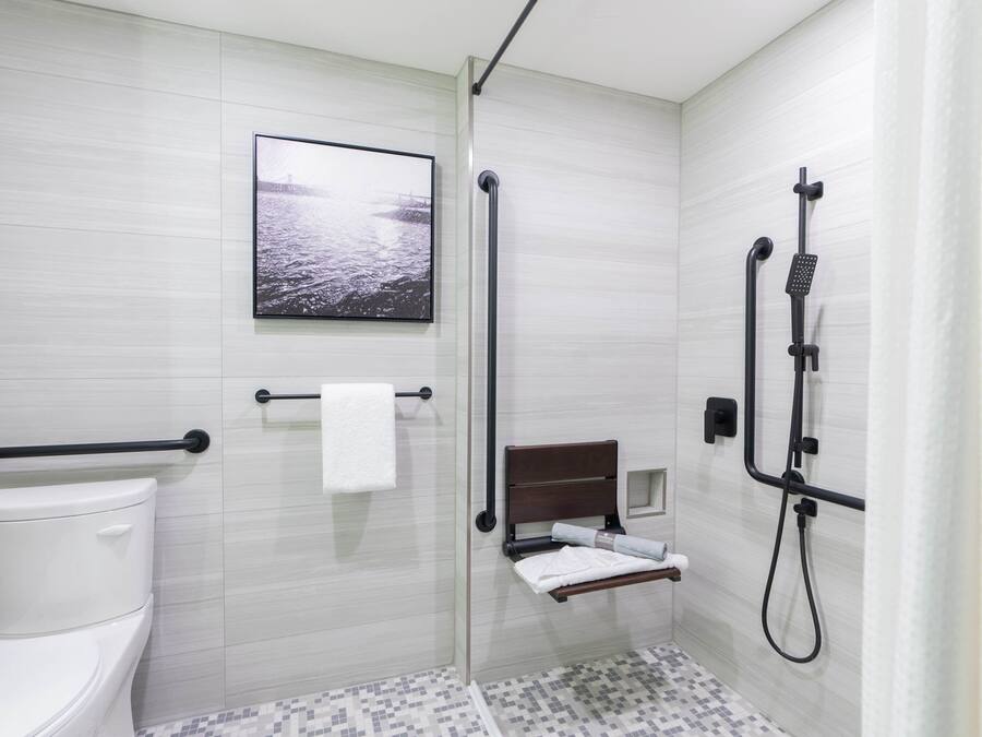 Ein modernes Badezimmer mit Toilette, einer Dusche inklusive Handbrause, einem Handtuchhalter und einem gerahmten Bild an der Wand.