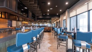 Un restaurante moderno con asientos de bar azules, una zona de cocina y ventanas amplias.