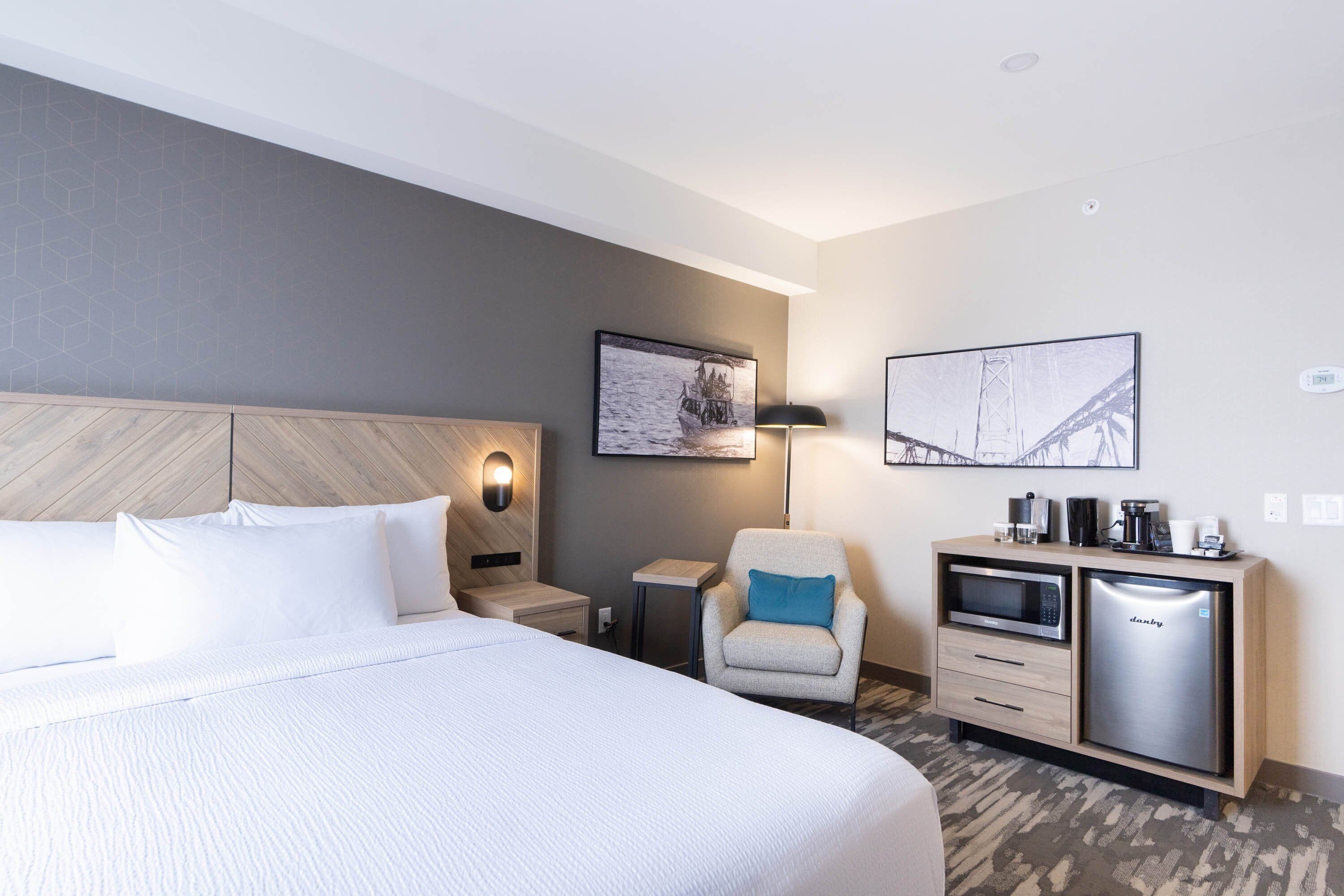 Una habitación de hotel con cama, una silla, escritorio con microondas y refrigerador.