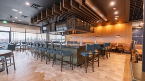 Un restaurante moderno con suelo de patrón hexagonal, paneles de techo de madera y una zona de bar con taburetes.