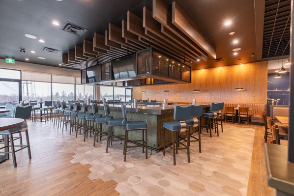 Un restaurante moderno con suelo de patrón hexagonal, paneles de techo de madera y una zona de bar con taburetes.