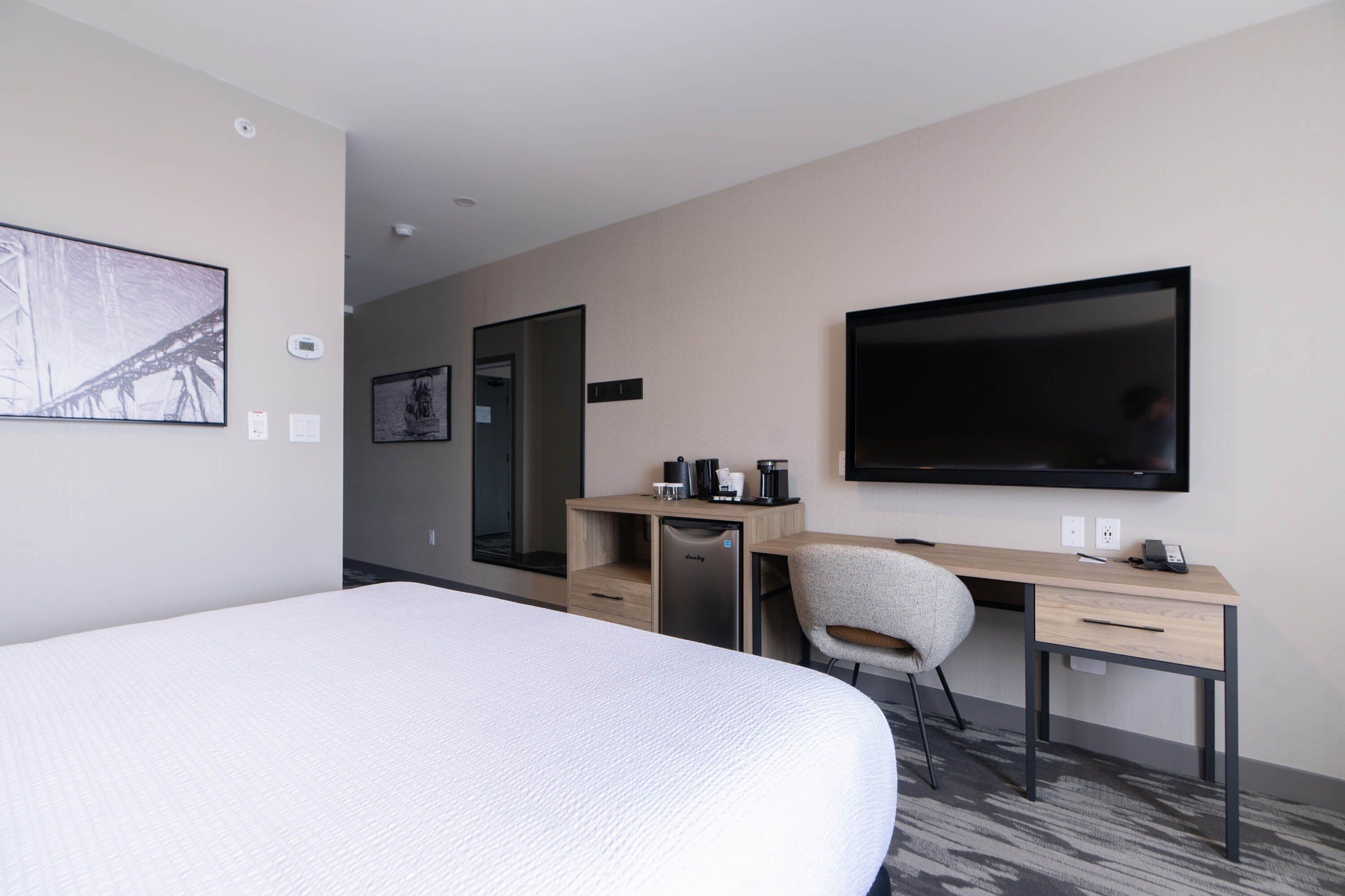 Habitación de hotel con una cama grande, un escritorio con silla, un televisor de pantalla plana y una cafetera.