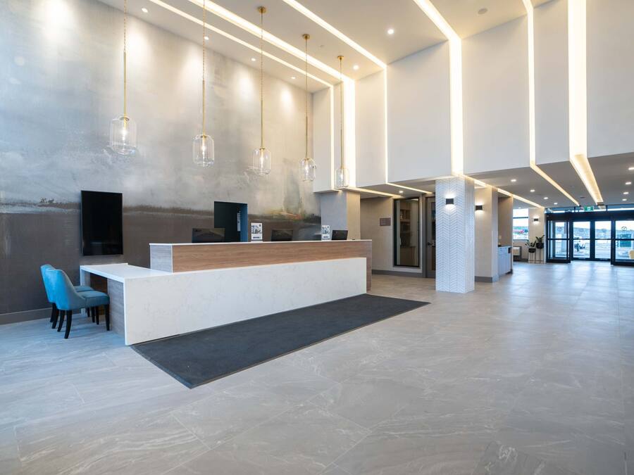 Un área de recepción moderna con mostrador, asientos, iluminación colgante y vistas al acceso.
