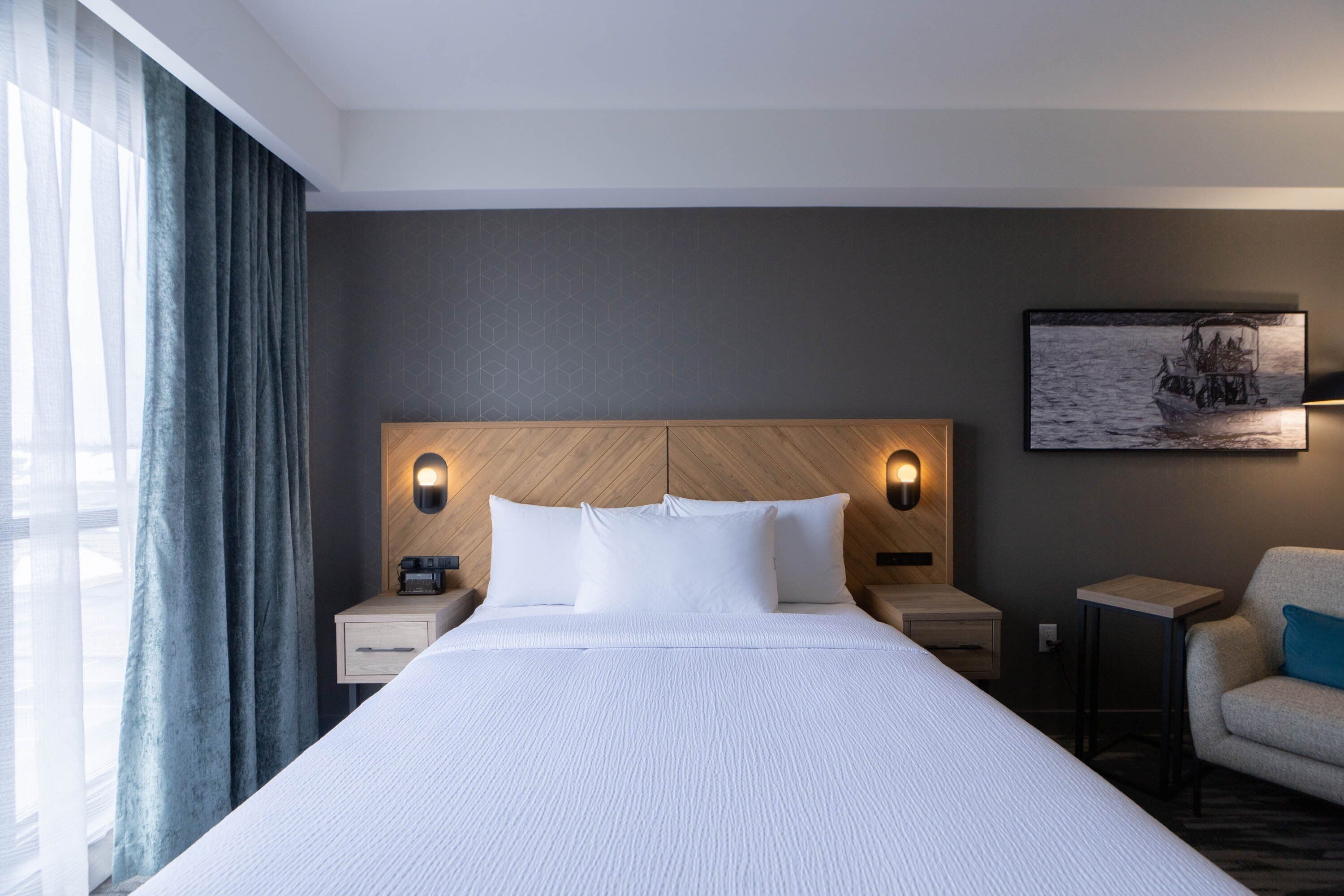 A hotel room with a large bed, two bedside tables, a nightstand, a chair, and a painting on the wall.