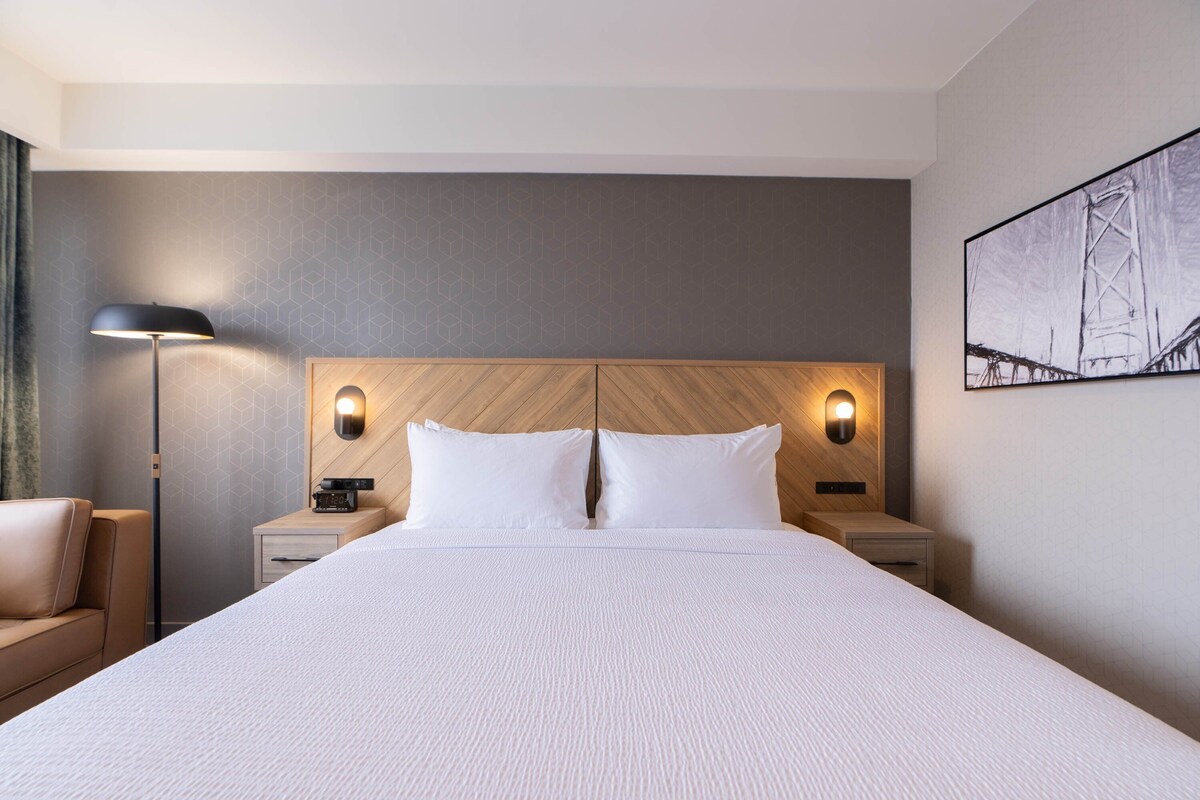 Habitación de hotel con una cama grande, dos mesitas de noche, una lámpara y un cuadro en la pared.