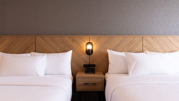 Habitación de hotel con dos camas, cabecero de madera, mesita de noche con un reloj y pared con diseño geométrico.