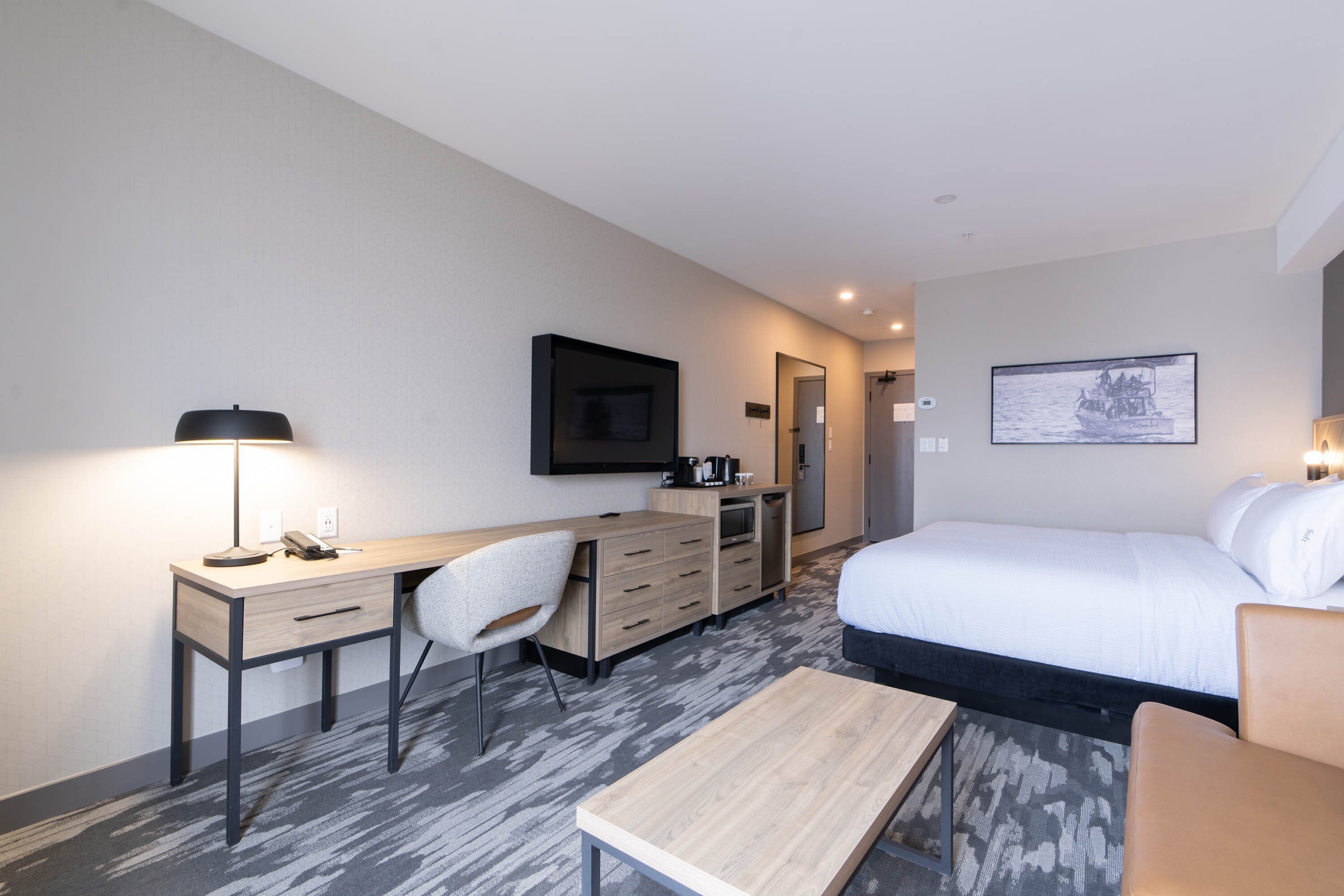 A hotel room with a bed, desk, chair, and a small table.
