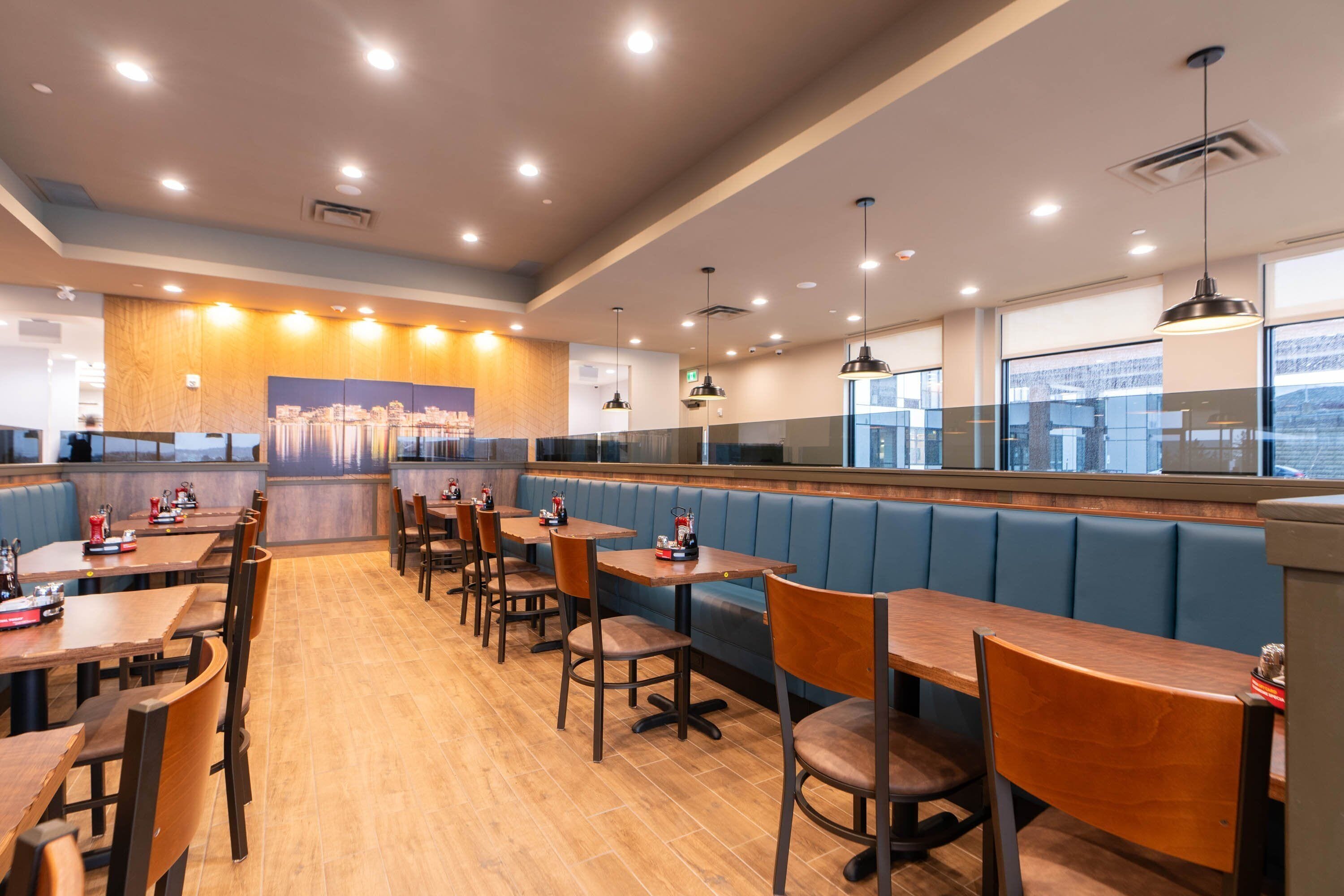 A restaurant with booths and tables, wooden flooring, and pendant lighting.
