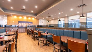 A restaurant with booths and tables, wooden flooring, and pendant lighting.