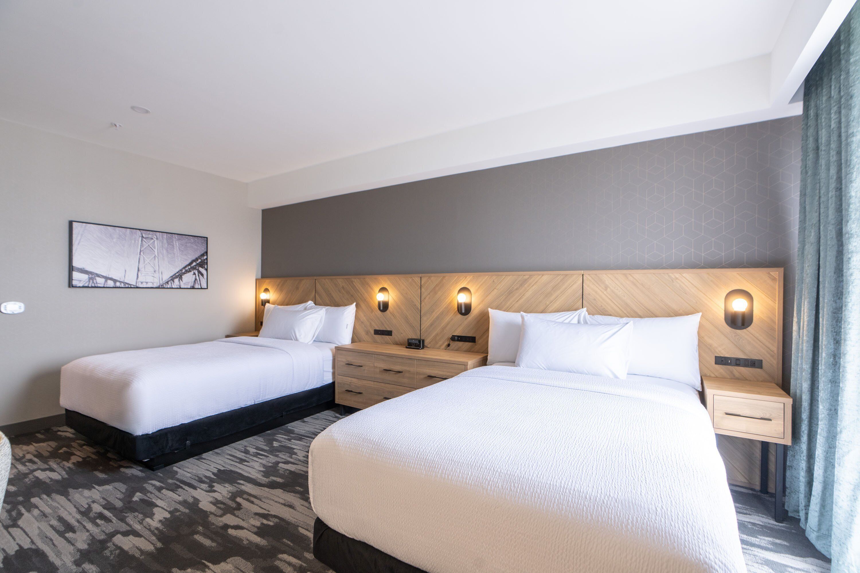 Een hotelkamer met twee bedden, een houten hoofdbord, wandlampen, een klein bureau en een vloerbedekking.