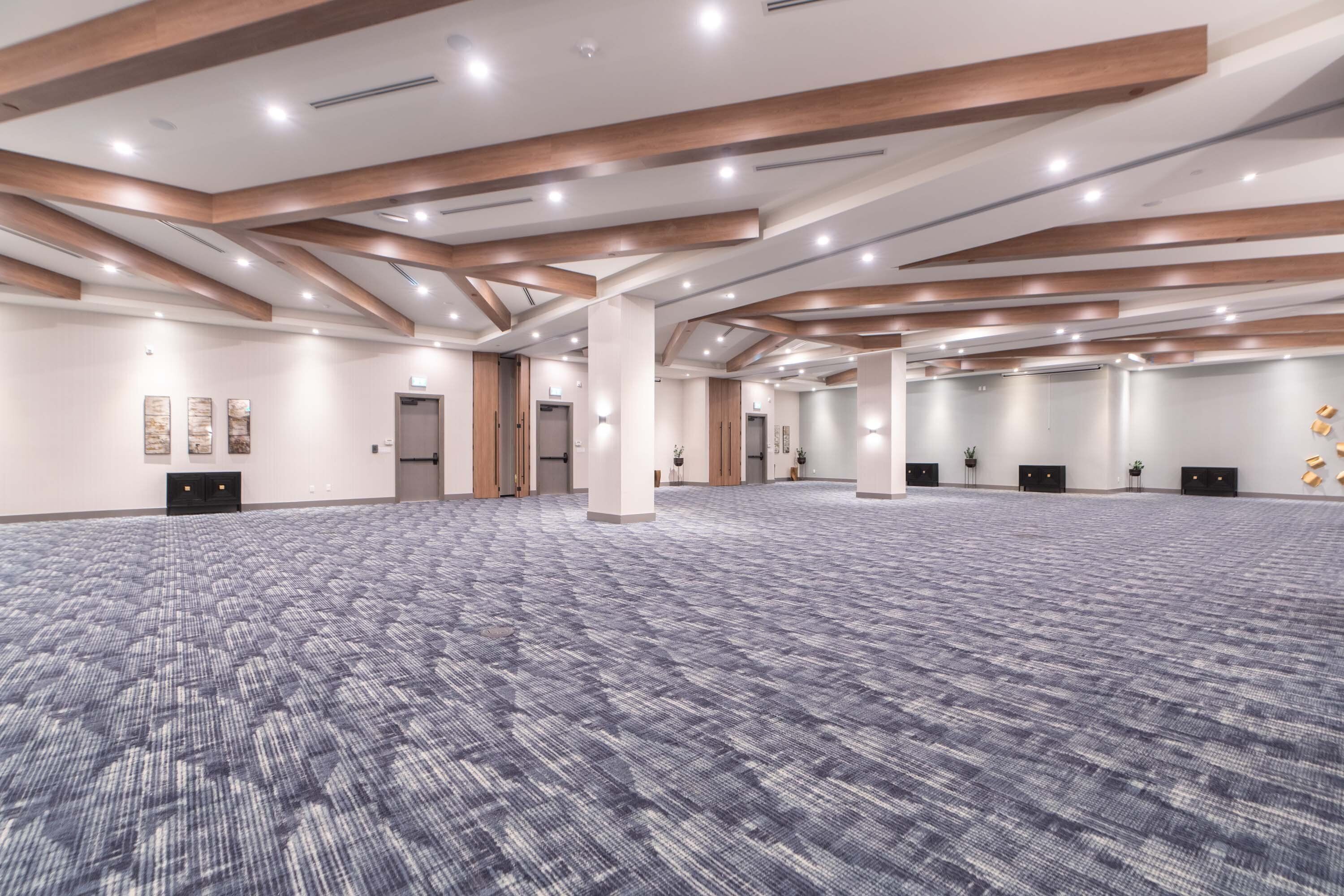 A spacious conference room with a patterned carpet, wooden beams, and recessed lighting.