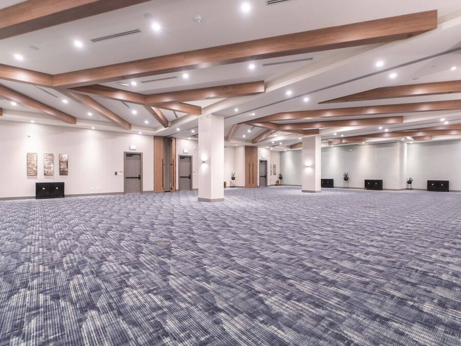 A spacious conference room with a patterned carpet, wooden beams, and recessed lighting.
