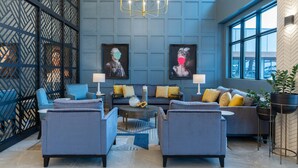 Un área de lounge moderna con una paleta de colores azul y gris, que incluye un sofá, sillones, una mesa de centro y una araña.