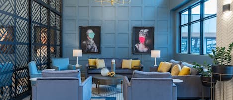 A modern lounge area with a blue and gray color scheme, featuring a sofa set, armchairs, a coffee table, and a chandelier.