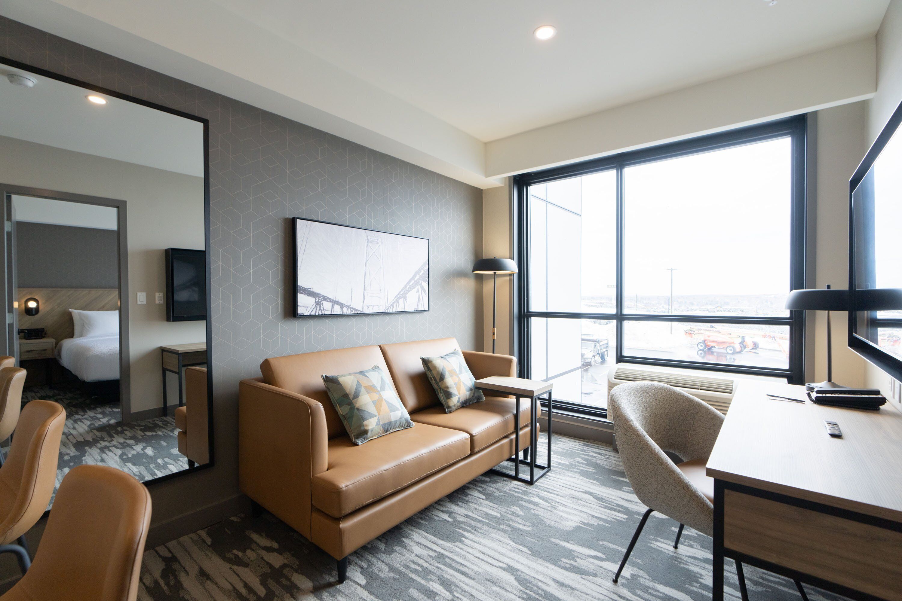 Una habitación de hotel moderna con sofá de cuero, un escritorio y un amplio ventanal con vistas a la ciudad.