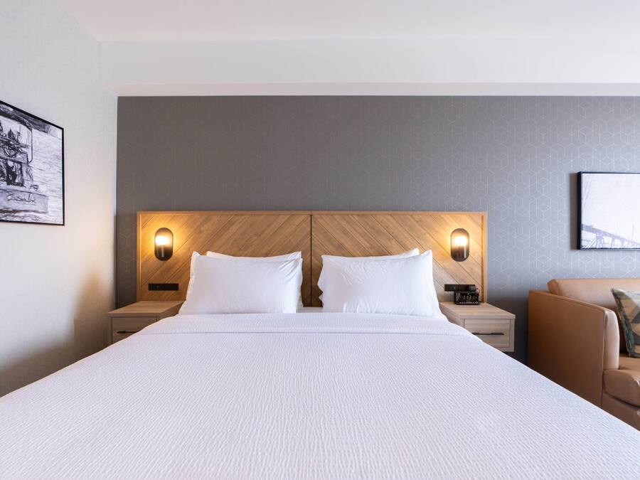 A hotel room with a large bed, two bedside tables with lamps, a wooden headboard, and a couch with a pillow.
