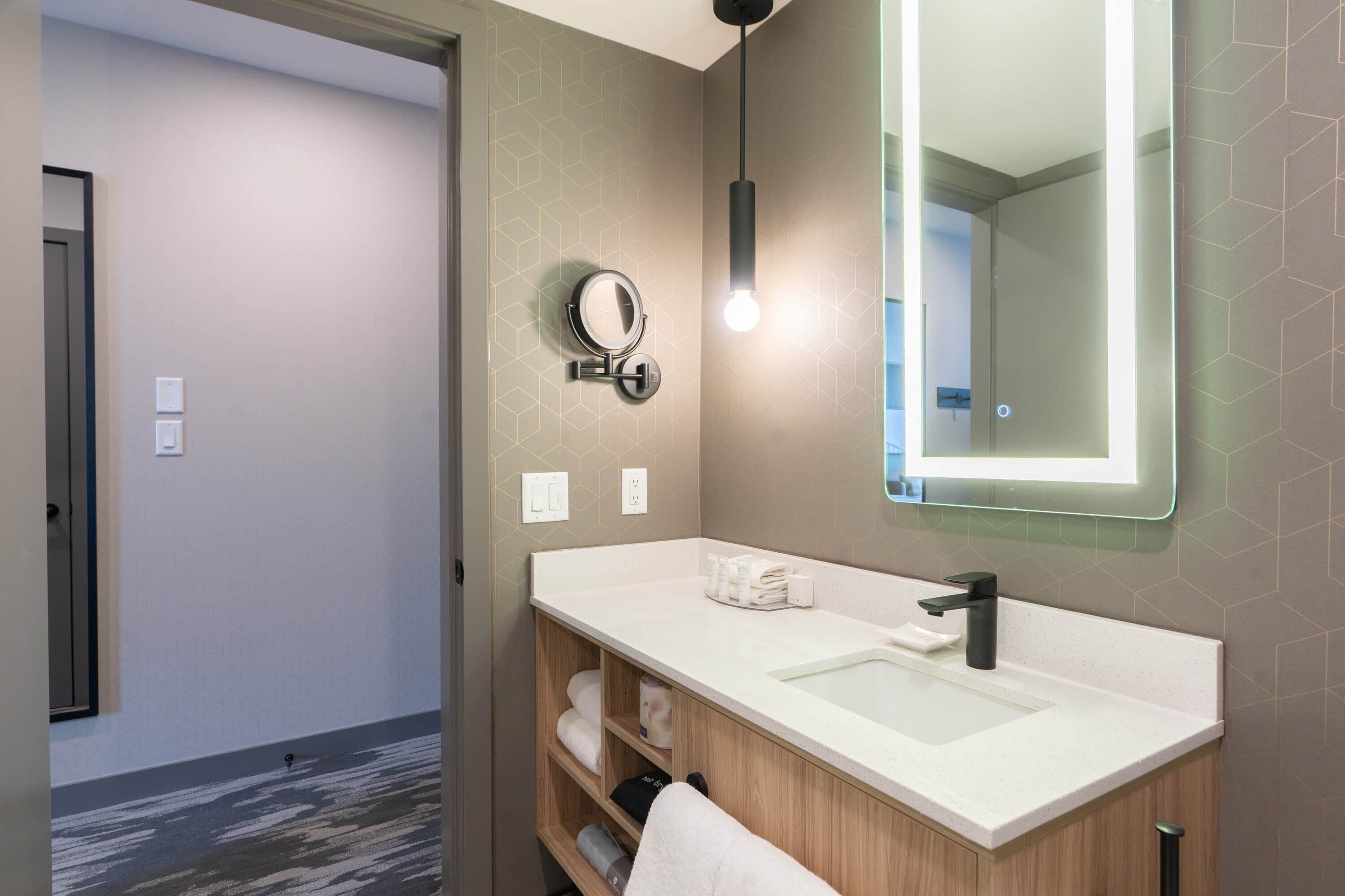 A modern bathroom with a white sink, a round mirror, and a pendant light.