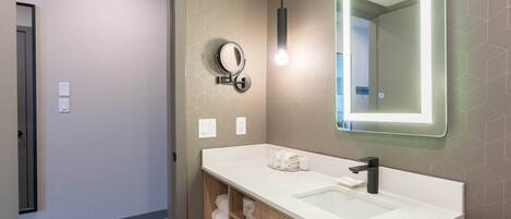 A modern bathroom with a white sink, a round mirror, and a pendant light.
