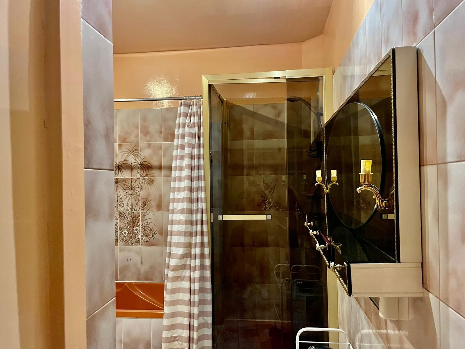 A modern bathroom with a glass shower enclosure, a striped shower curtain, and a vanity with a mirror and two sconces.