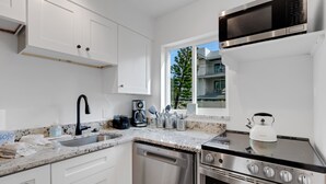 A modern kitchen with white cabinets, stainless steel appliances, a dishwasher, a stove, and a microwave. - Charming Beach Condo Steps to Beach | Heated Pool | Sleeps 4 (Bradenton Beach)