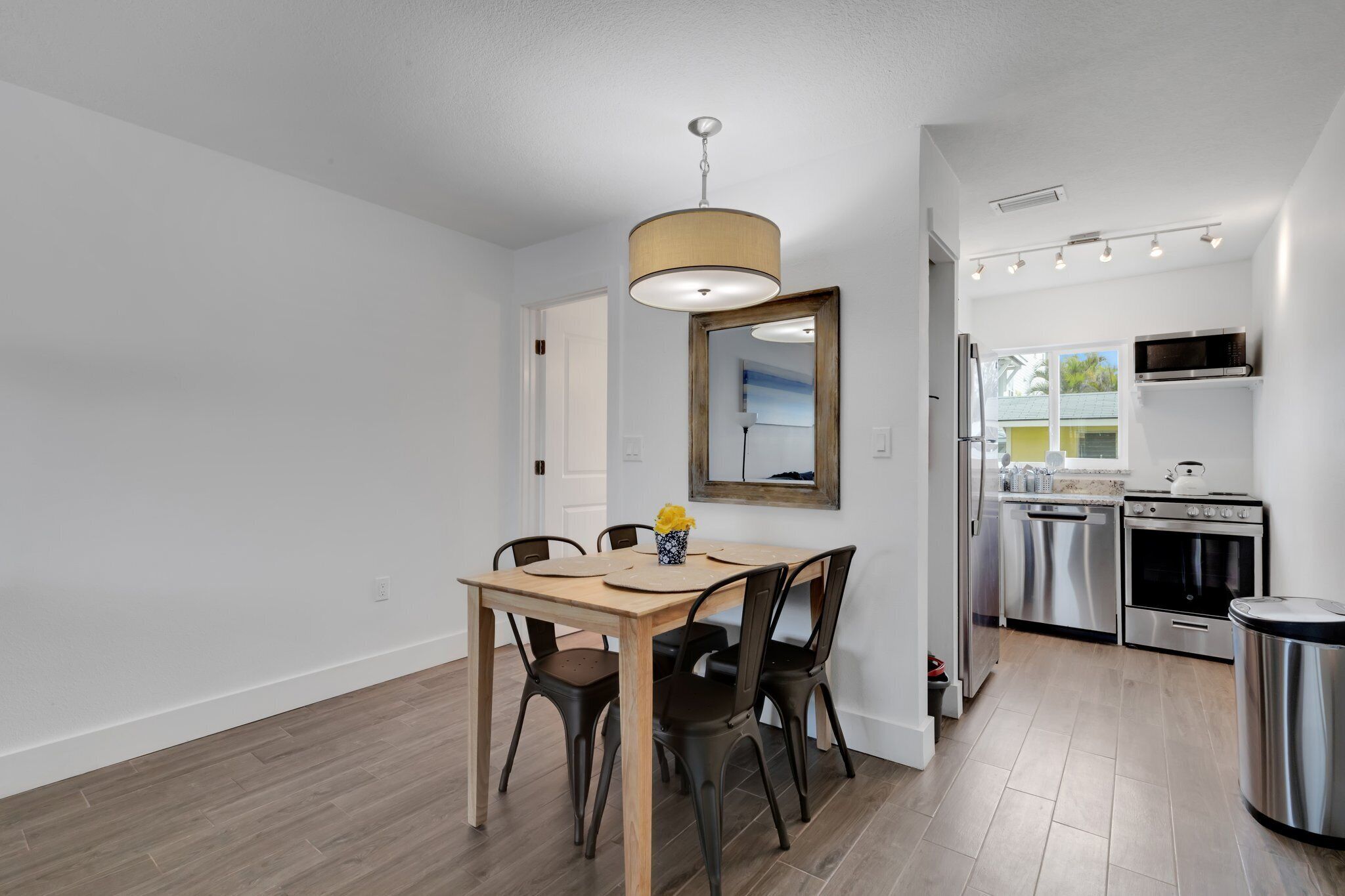 Une cuisine moderne dotée d’appareils électroménagers en acier inoxydable, un coin repas avec une table et des chaises en bois, et un luminaire suspendu au-dessus de la table.